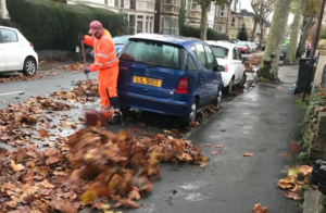 A man in hi-vis sweeps leaves on a Bristol street